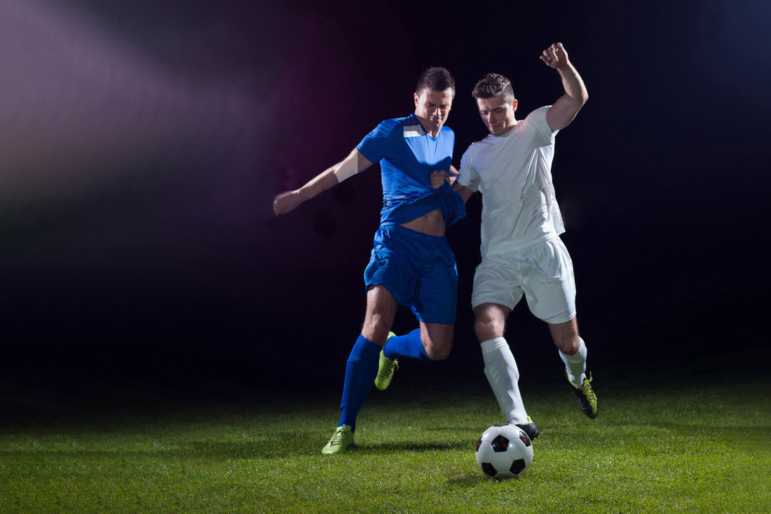 Zwei Männer spielen Fußball auf einem beleuchteten Feld.