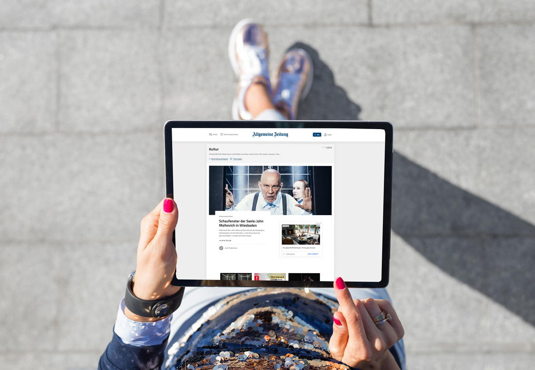 Eine Person hält ein Tablet, auf dem eine digitale Zeitung angezeigt wird.