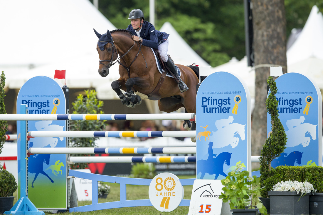 Eine Person reitet auf einem Pferd über ein Hindernis im LONGINES Pfingst Turnier. 