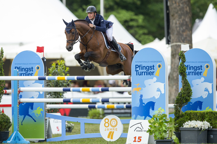 Eine Person reitet auf einem Pferd über ein Hindernis im LONGINES Pfingst Turnier. 