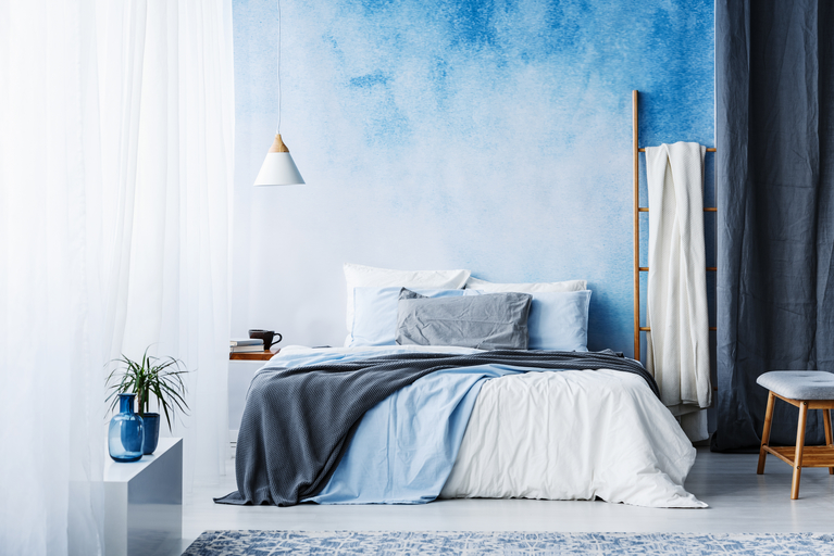 Ein Schlafzimmer mit blauer Wand und einem Bett in der Mitte des Raumes. 