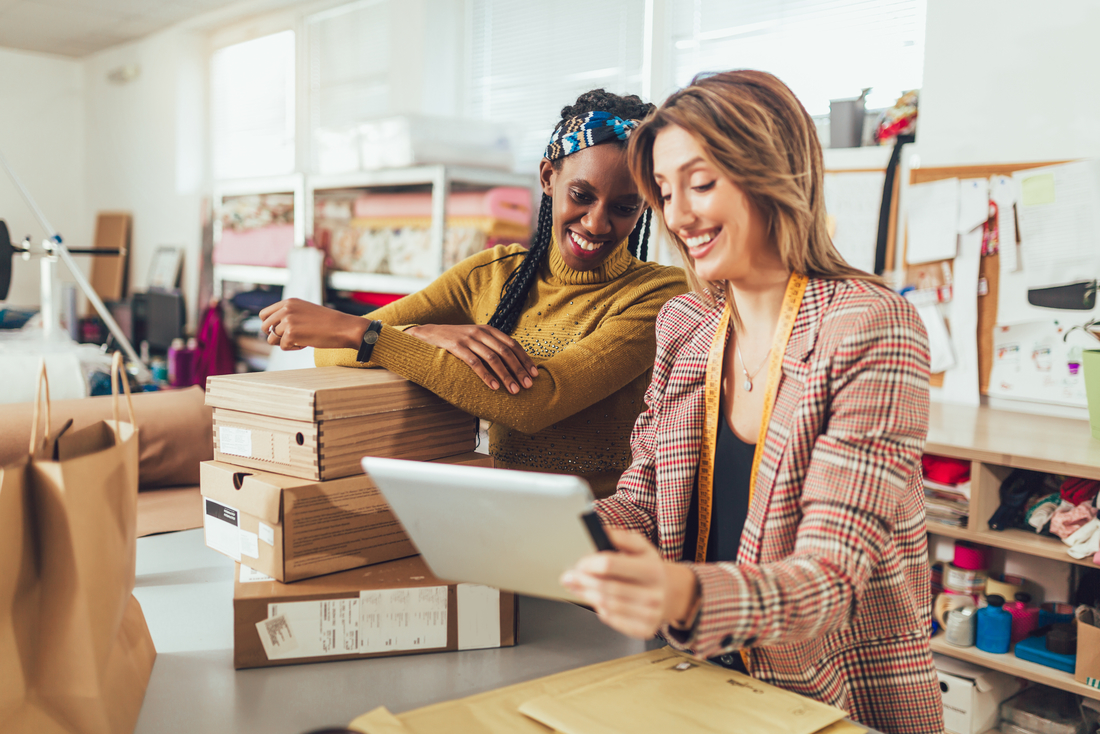 Zwei Frauen in einem Büro arbeiten gemeinsam an einem Tablet und diskutieren dabei ihre Ideen.