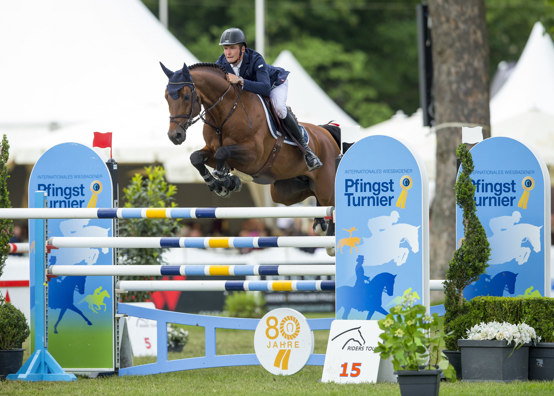 Eine Person reitet auf einem Pferd über ein Hindernis im LONGINES Pfingst Turnier. 