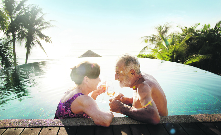 Ein älteres Paar entspannt sich und genießt ein Getränk im Pool im Urlaub.